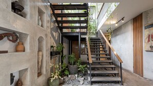 A narrow staircase with a wooden handrail, flanked by shelves with various decorative items and plants. - Kandarpa Ubud (Ubud)