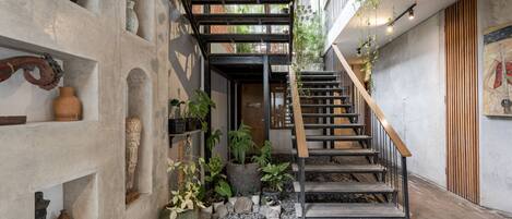 A narrow staircase with a wooden handrail, flanked by shelves with various decorative items and plants.