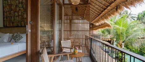 A balcony with wooden furniture, a hanging light fixture, and a view of a pool and palm trees.