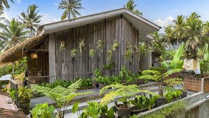 A wooden building with vertical slats, surrounded by lush tropical plants and palm trees. - Kandarpa Ubud (Ubud)