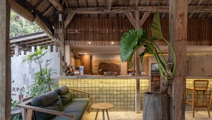 A cozy seating area with a sofa and a round table, a reception desk, and a large plant. - Kandarpa Ubud (Ubud)