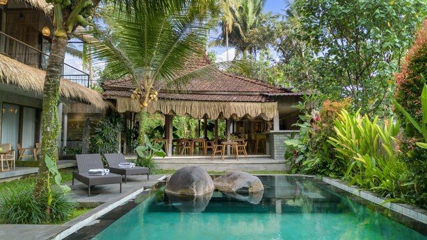 A pool area with lounge chairs, a thatched-roof structure, and lush greenery. - Kandarpa Ubud (Ubud)