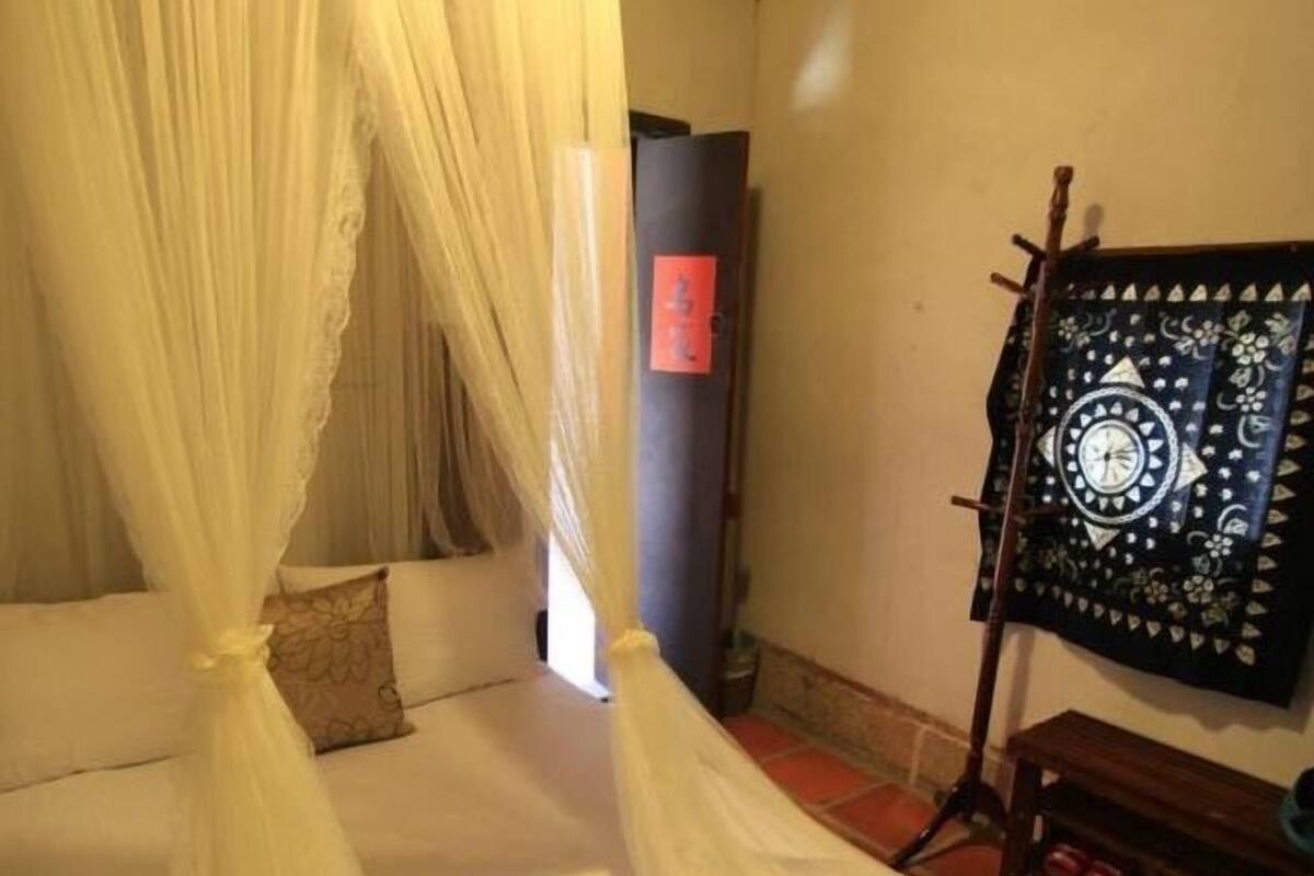 A room with a bed covered by a white canopy, a small table with a decorative item, and a wall-mounted artwork.