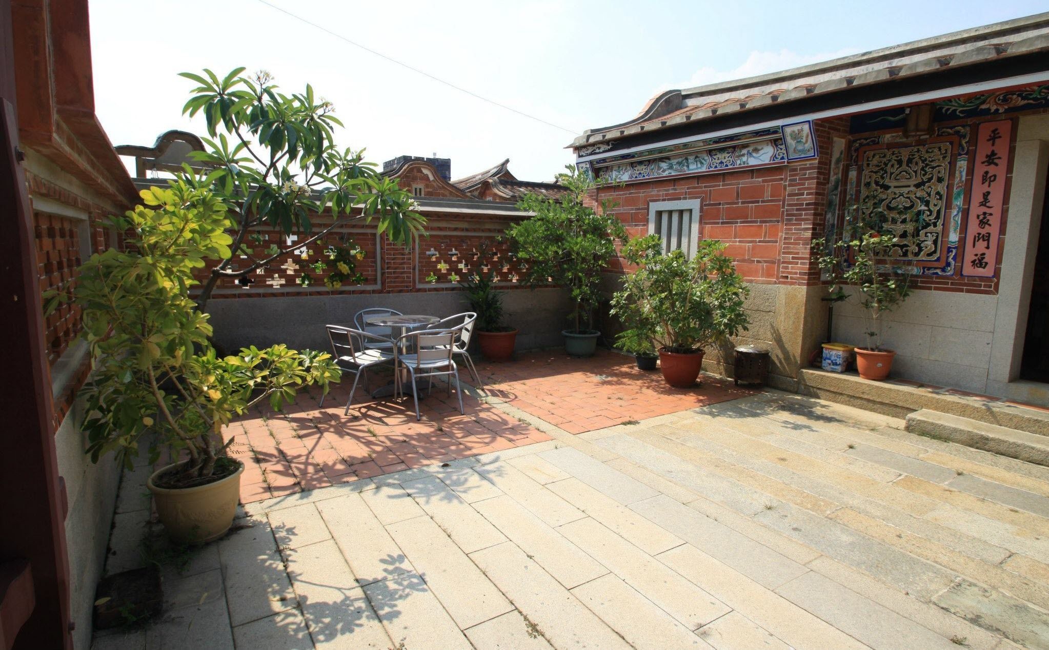 A courtyard with a brick wall, potted plants, and a traditional tiled roof.