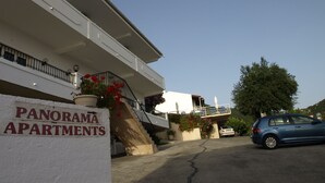 A building labeled "PANORAMA APARTMENTS" with a staircase, a car parked in front, and a clear sky.