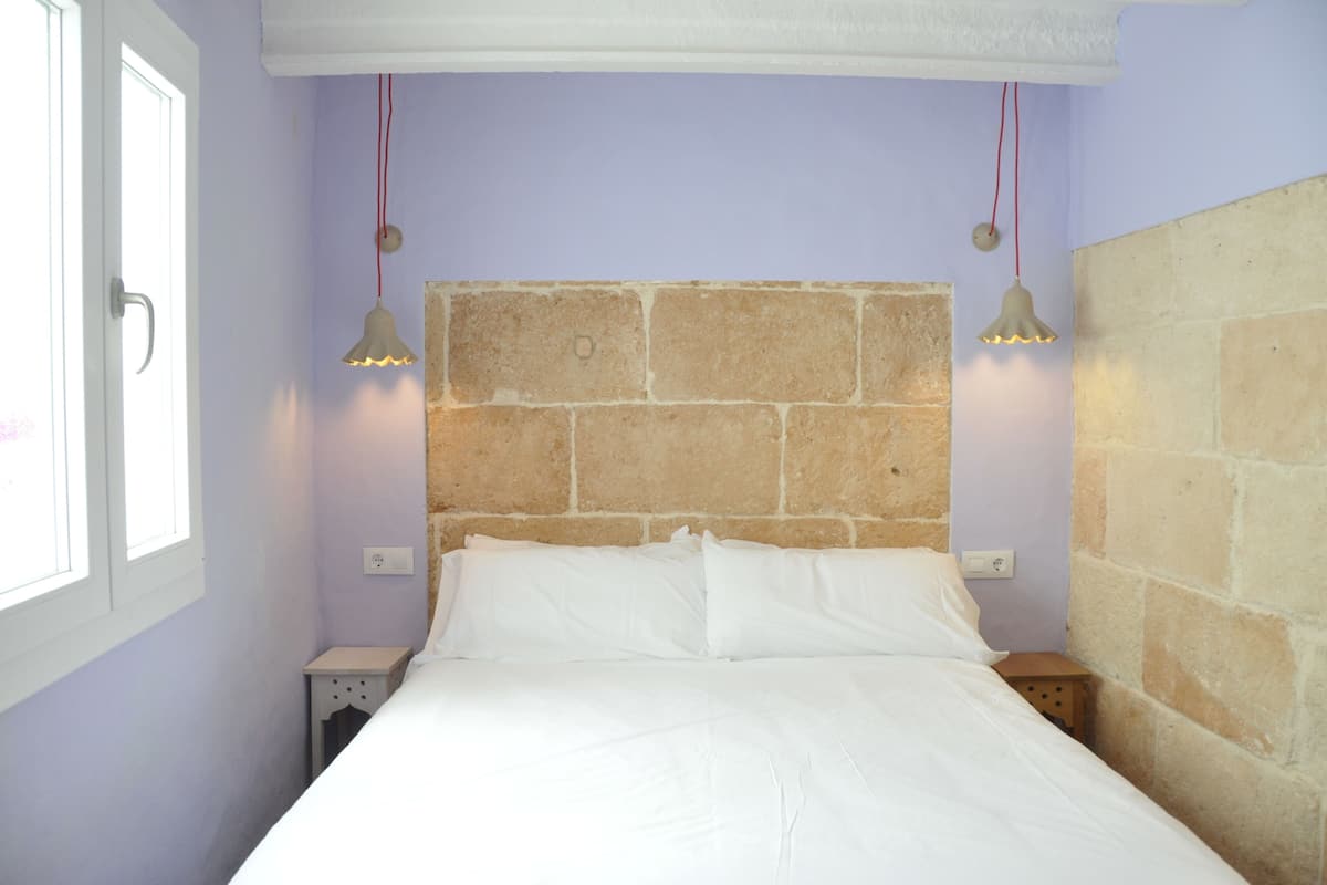 A bedroom with a stone headboard, white bedding, two bedside lamps, and a nightstand.