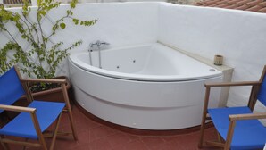 A corner bathtub with two blue cushioned chairs, a potted plant, and a tiled floor. - Rifugio Azul (Ciutadella de Menorca)