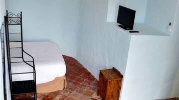 A small, narrow room with a bed, a wooden stool, and a television on a white stand.