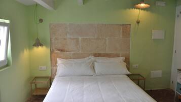 Un dormitorio con cabecera de piedra, una cama con ropa blanca, dos mesitas de noche y dos lámparas de pared.