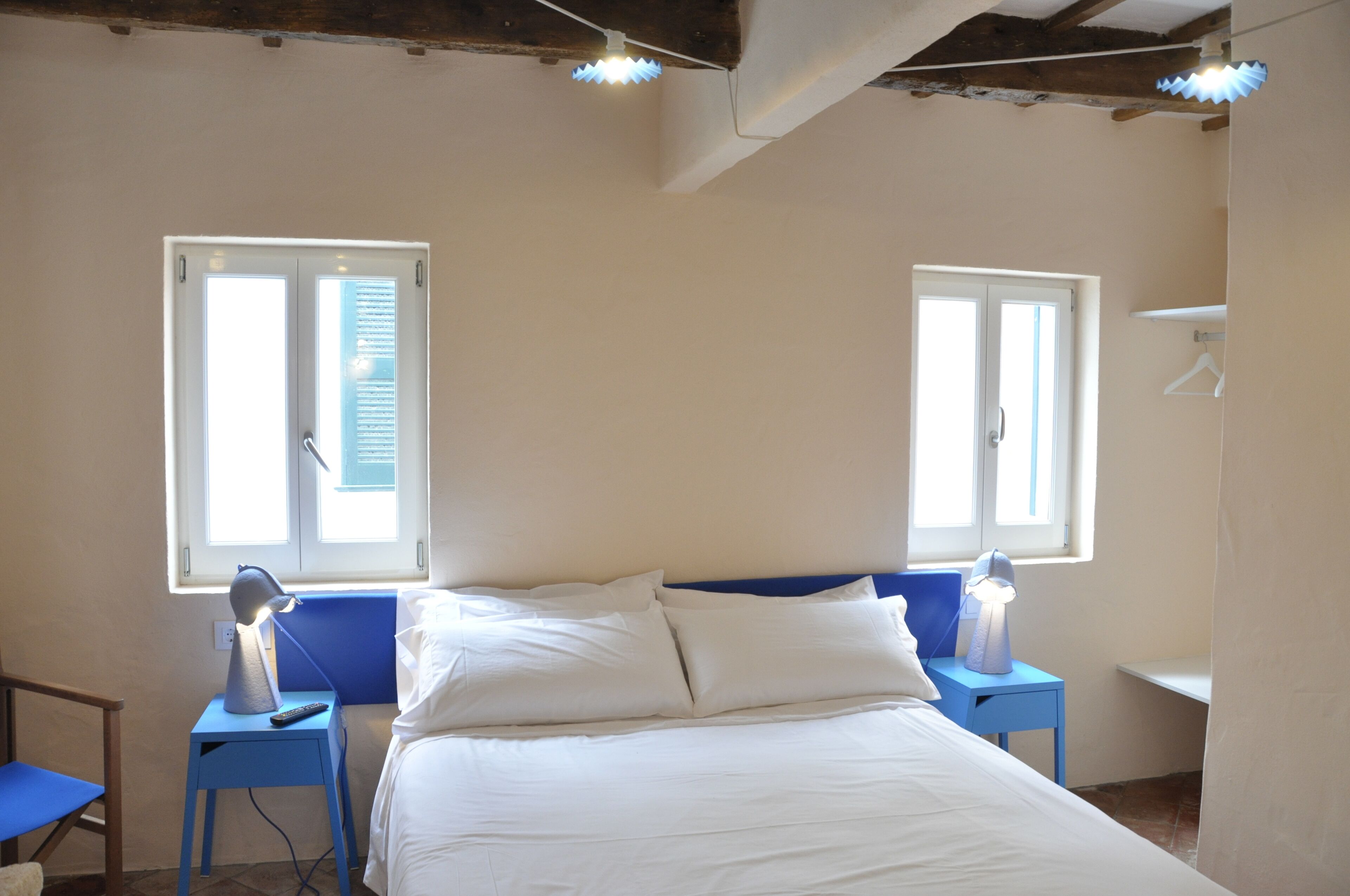 A bedroom with a bed, two bedside tables with lamps, a chair, and two windows with blinds.