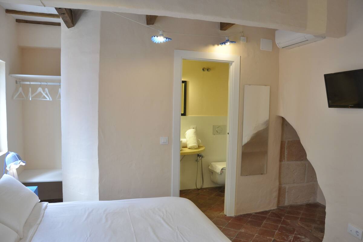 A bedroom with a bed, a bathroom with a shower, and a TV mounted on the wall.