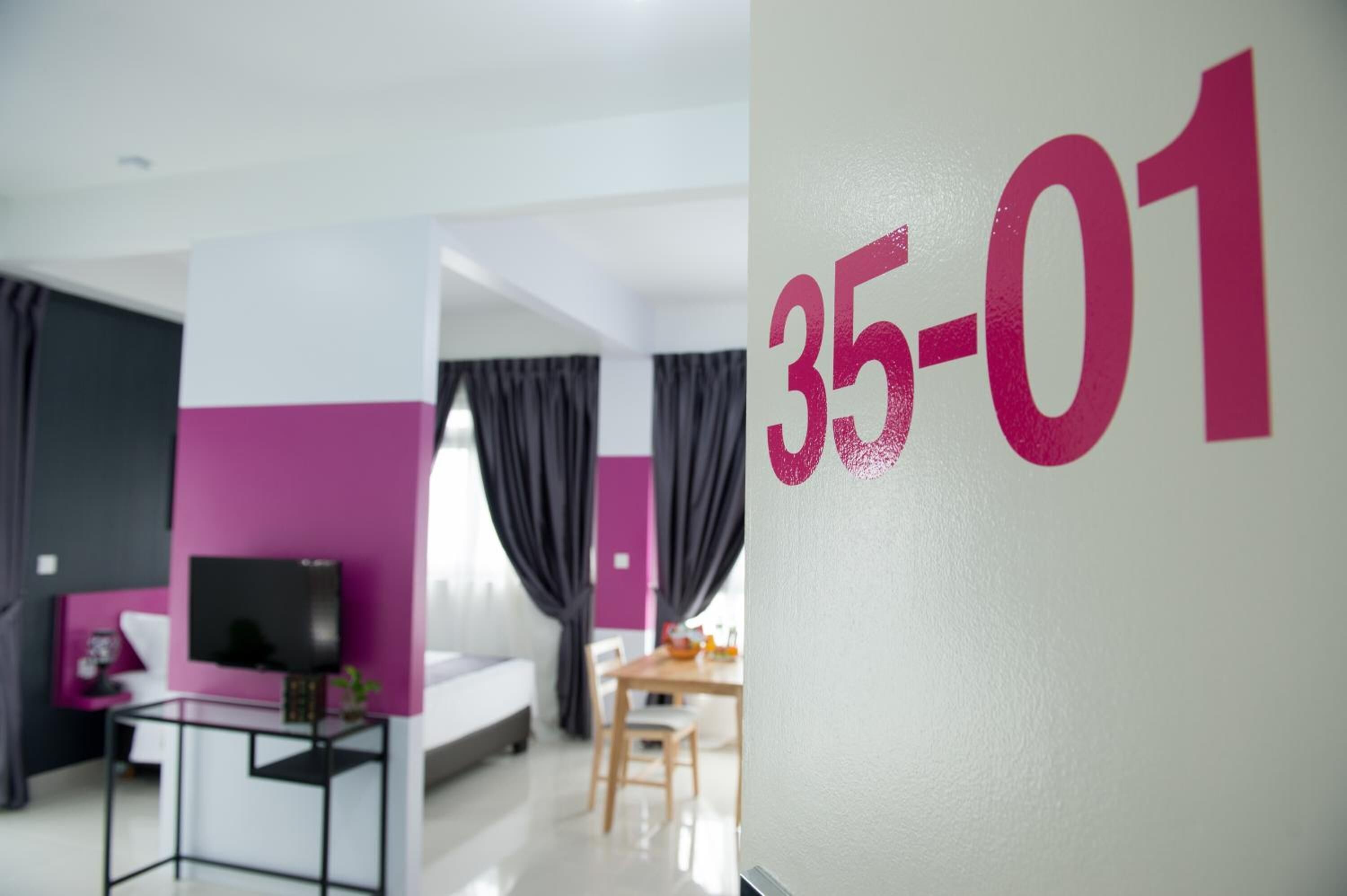 Een moderne hotelkamer met een bed, een televisie op een standaard, een kleine tafel en een zithoek met een tafel en stoelen.