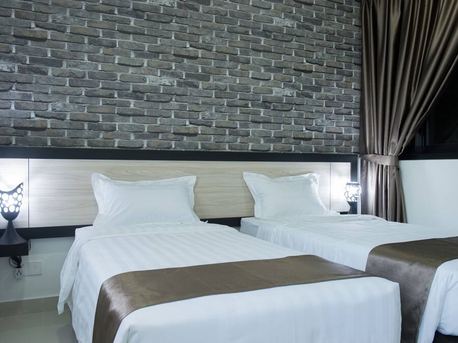 Una habitación de hotel con dos camas, un muro de ladrillo, un cabecero de madera, una mesita de noche con una lámpara y una ventana con cortinas.