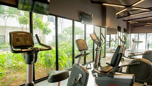 A gym with cardio machines, weight machines, and a large window with a view of greenery. - Ezzyhome Medini (Iskandar Puteri)