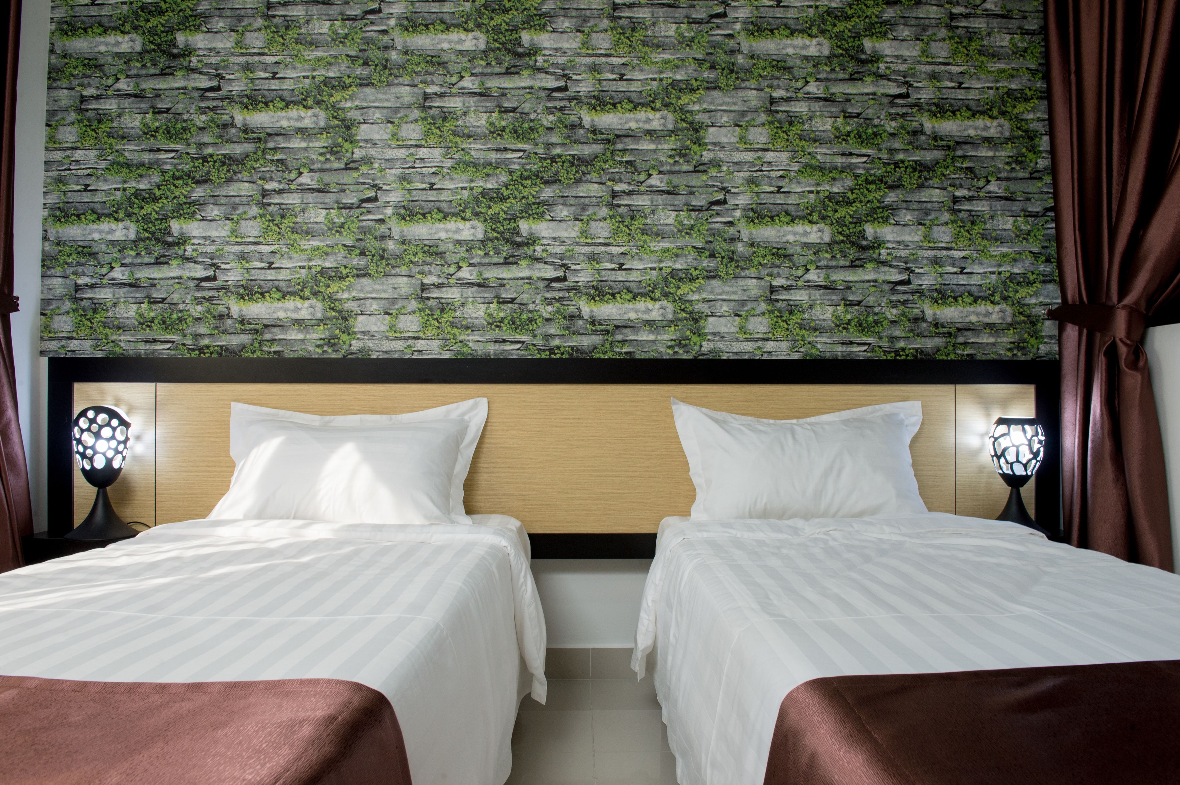 Ett hotellrum med två sängar, en vägg av sten med växter och två sänglampor.