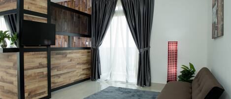 Una sala de estar moderna con una pared de acento de madera, un sofá gris, un tapete azul y un ventanal con cortinas traslúcidas.