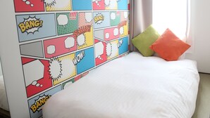 Ein Schlafzimmer mit farbenfroher Wandkunst im Comic-Stil, einem weißen Bett und zwei Kissen.