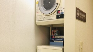 Eine Münzwaschmaschine mit einem darüber platzierten, stapelbaren Trockner und einer Waschmaschine, neben einem kleinen Kühlschrank.