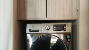 A compact, stainless steel front-loading washing machine with a digital control panel, housed in a wooden cabinet with a tiled floor. - Cozy Flat near Athens City Center (Athens)