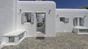 Un bâtiment aux murs blancs, doté d’une cour dallée de pierres, une porte donnant sur un espace intérieur et un petit banc.