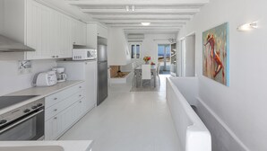 Une cuisine moderne avec des meubles blancs, un coin repas comprenant une table et des chaises, et une vue sur l’océan par les fenêtres.
