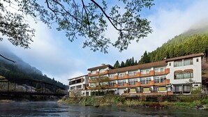 Ein mehrstöckiges Hotel mit Blick auf einen Fluss, einer Brücke und einen bewaldeten Hügel.