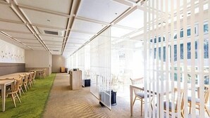 A modern interior with a long corridor, wooden tables, chairs, and a green carpet. - Myoken Onsen Nemu (Kirishima)