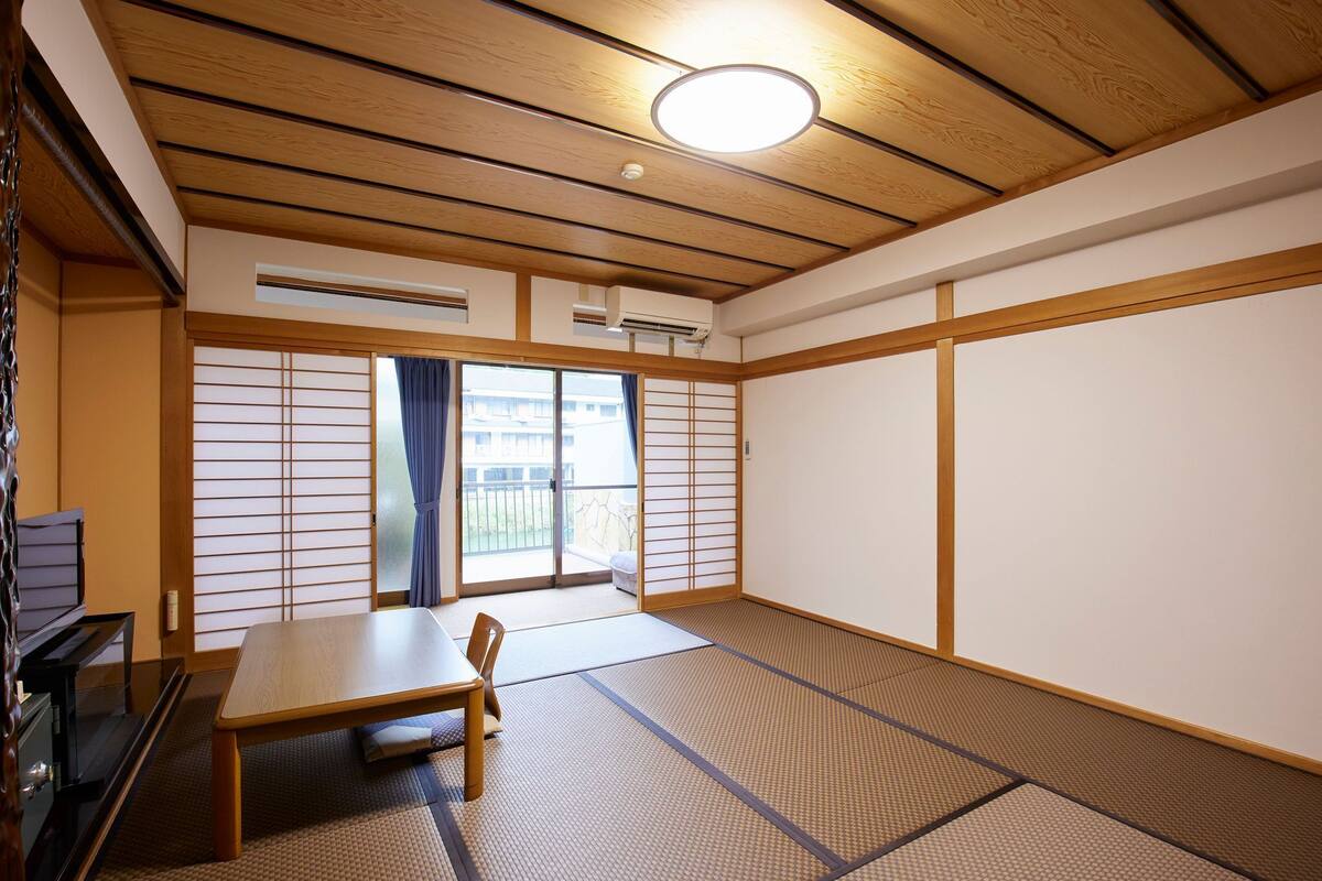 A traditional Japanese room with tatami flooring, a sliding door, a table, and a television.