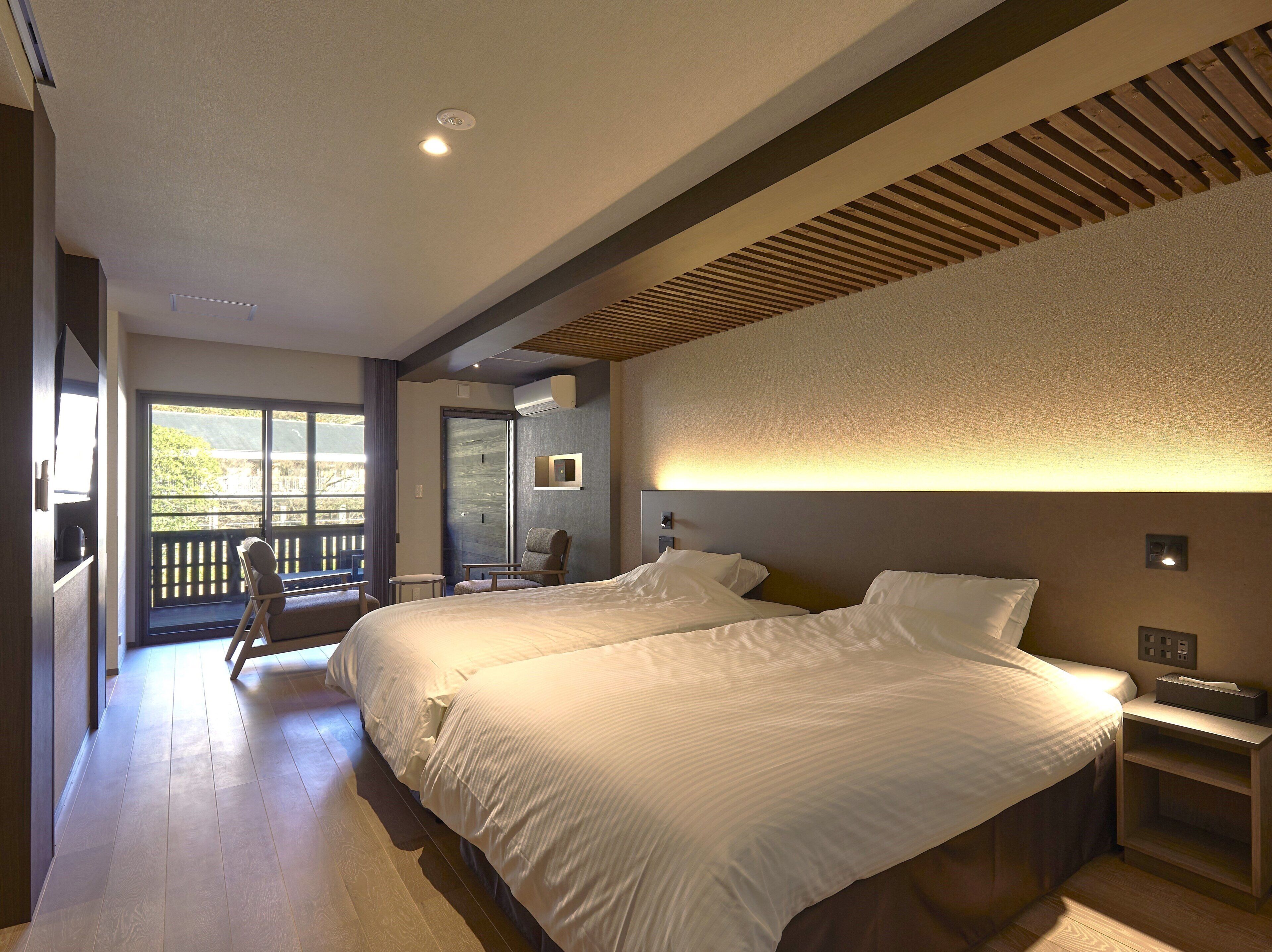 A hotel room with two beds, a balcony, a chair, and a desk.