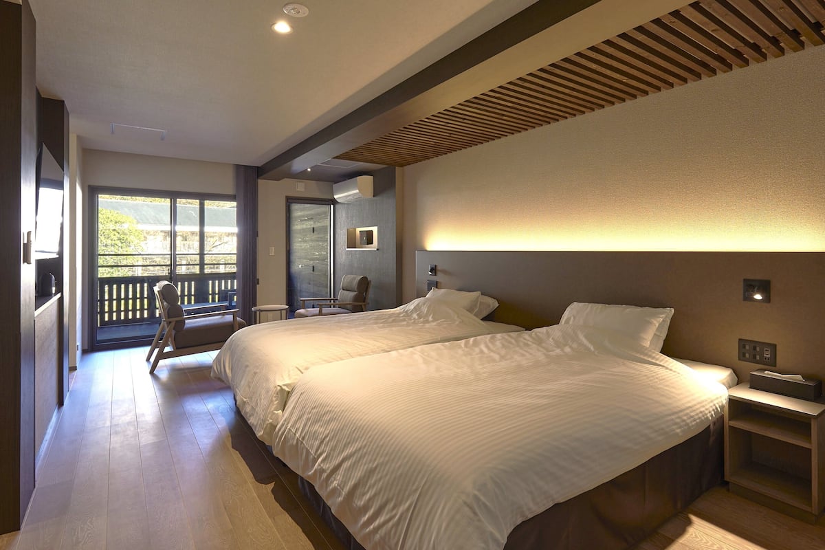 A hotel room with two beds, a balcony, a chair, and a desk.