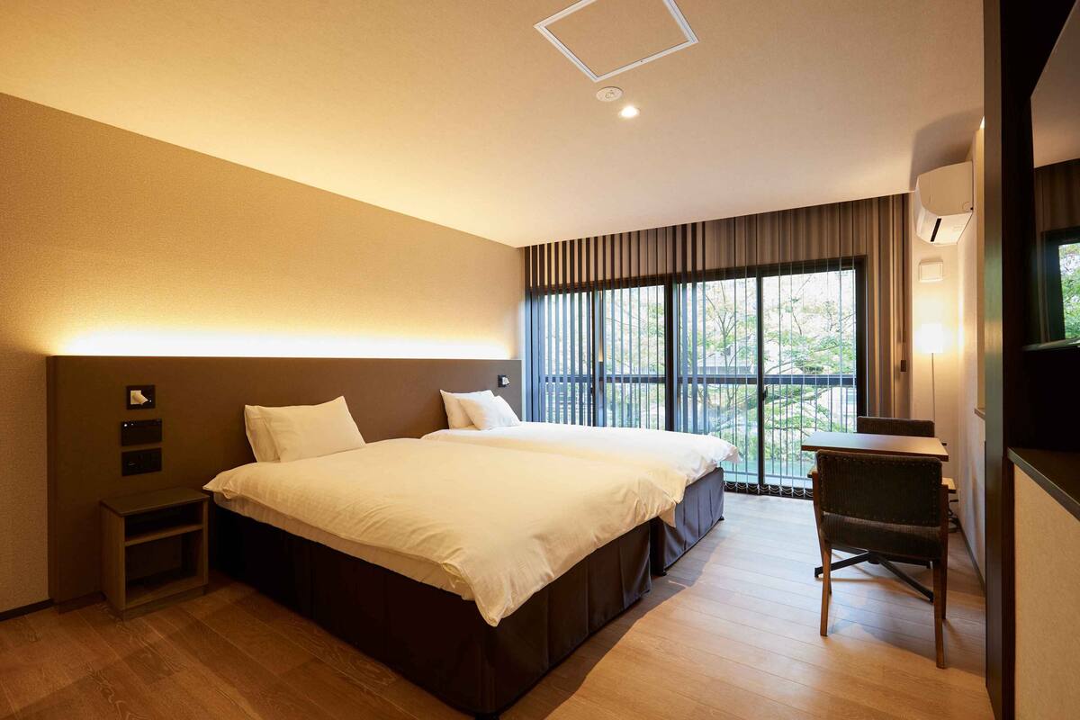 A modern hotel room with a large bed, a desk, and a view through the window.