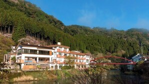 A multi-story building with balconies, a river, and a red bridge. - Myoken Onsen Nemu (Kirishima)