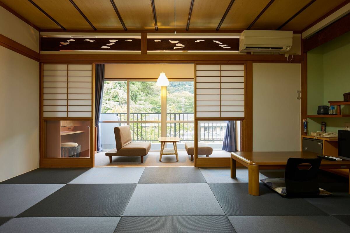 A tatami mat room with a sliding door, tatami mats, a sofa, a table, and a lamp.