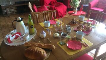 A dining table set with food and drinks, surrounded by wicker chairs and a red sofa.
