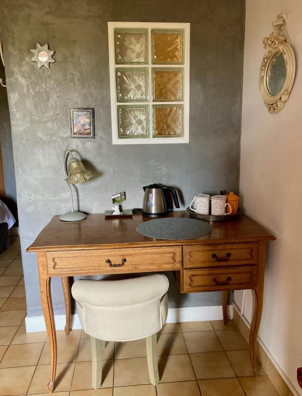 Een houten bureau met een stoel, een raam met decoratieve glasramen, een waterkoker, mokken en een klein, lijstwerk afgewerkt foto aan de muur.
