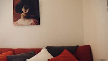A red sofa with multiple cushions, a small table with a candle, and a framed picture on the wall.