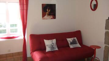 A red sofa with two decorative pillows, a small round table, a wall-mounted mirror, and a window with red curtains.