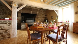 Un comedor con chimenea de piedra, sillas de madera, una mesa redonda y una araña.