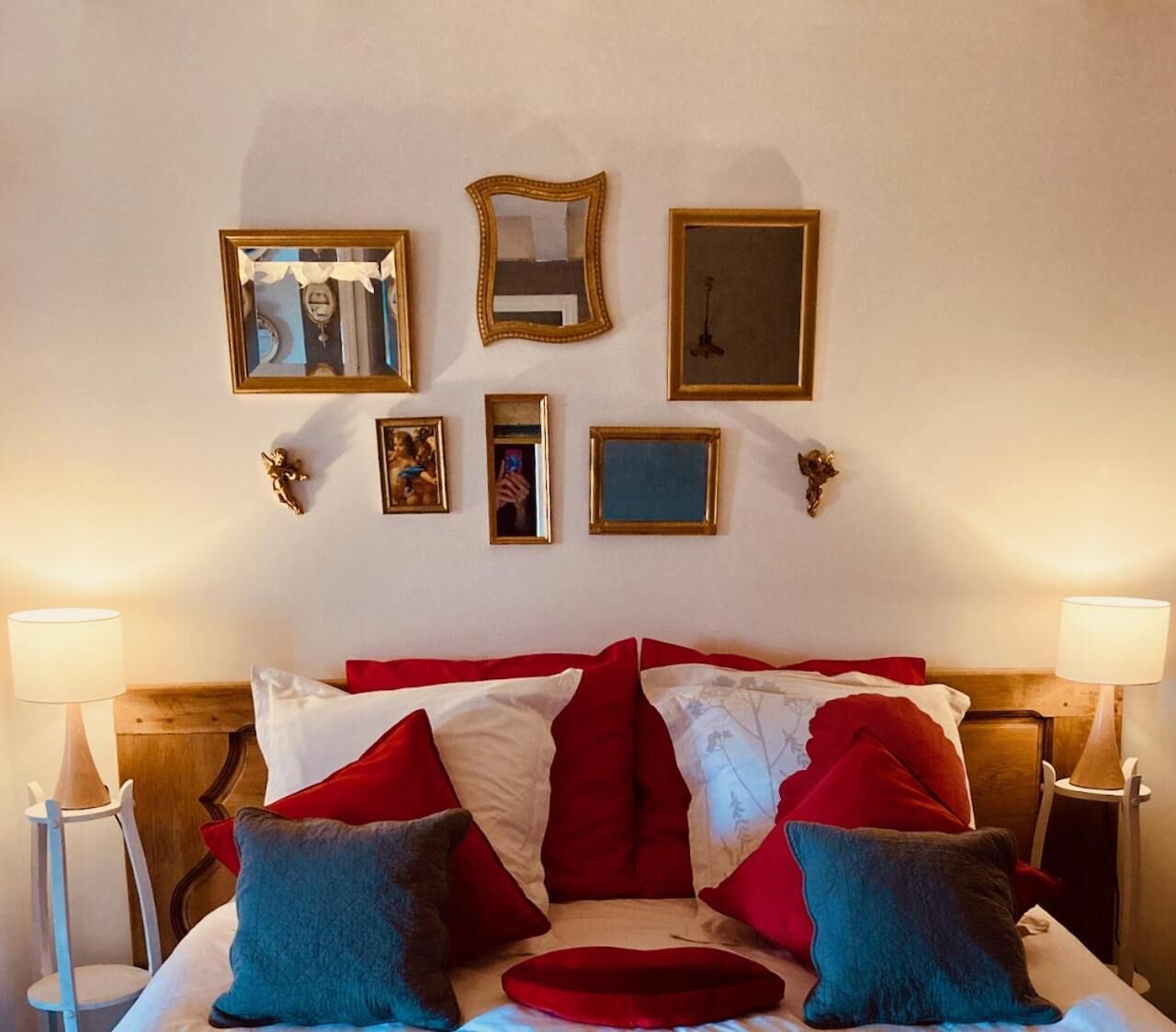 Een hotelkamer met een groot bed, rode en witte beddengoed, meerdere ingelijste foto's aan de muur en twee bedlampen.