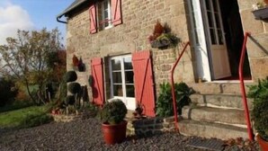 Una casa de piedra con contraventanas rojas, una puerta principal y un pequeño porche con escalones.