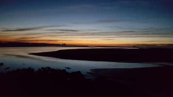 Paisaje plano con una masa de agua que refleja el cielo, una fuente de luz distante y una línea de horizonte.