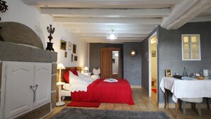 Un dormitorio con cama, mesitas de noche, cómoda, espejo y una puerta que da a otra habitación.