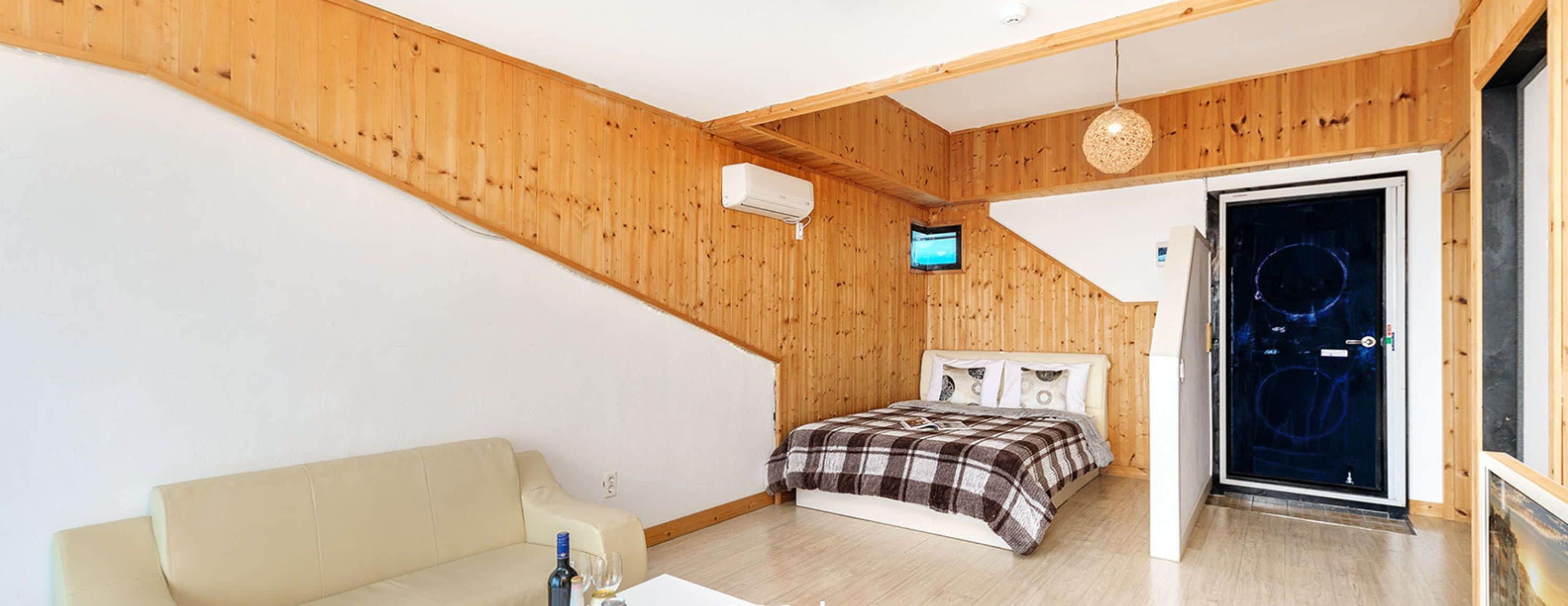A bedroom with a bed, a TV, a wooden ceiling, and a door leading to a balcony.