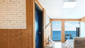 A bedroom with a bed, a wooden door, a window, and a view of the ocean.