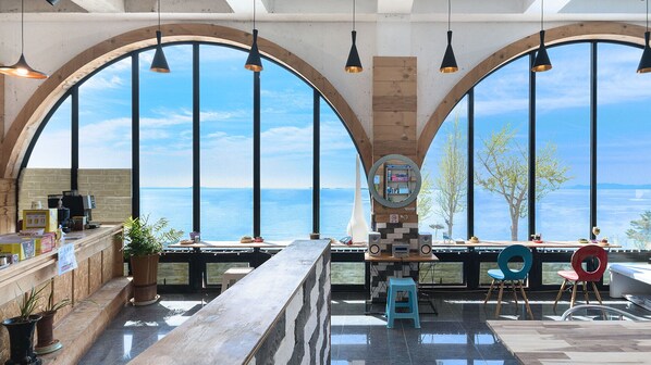 A spacious room with large arched windows offering a view of the sea, a wooden bar area, and a seating area with chairs and a table.