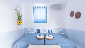 Een slaapkamer met twee bedden, een plafondventilator, een airconditioner, een raam met blauwe gordijnen, een aan de muur bevestigde plant en twee geweven decoraties aan de wand.
