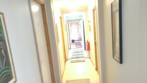A narrow hallway with a carpet, framed artwork on the walls, and a fire extinguisher mounted on the wall. - Holandsvika Bomiljø (Vefsn)