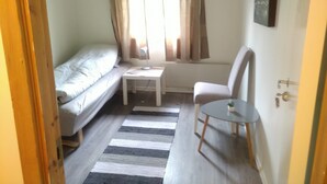 A small, compact room with a bed, a chair, a small table, and a window with curtains. - Holandsvika Bomiljø (Vefsn)