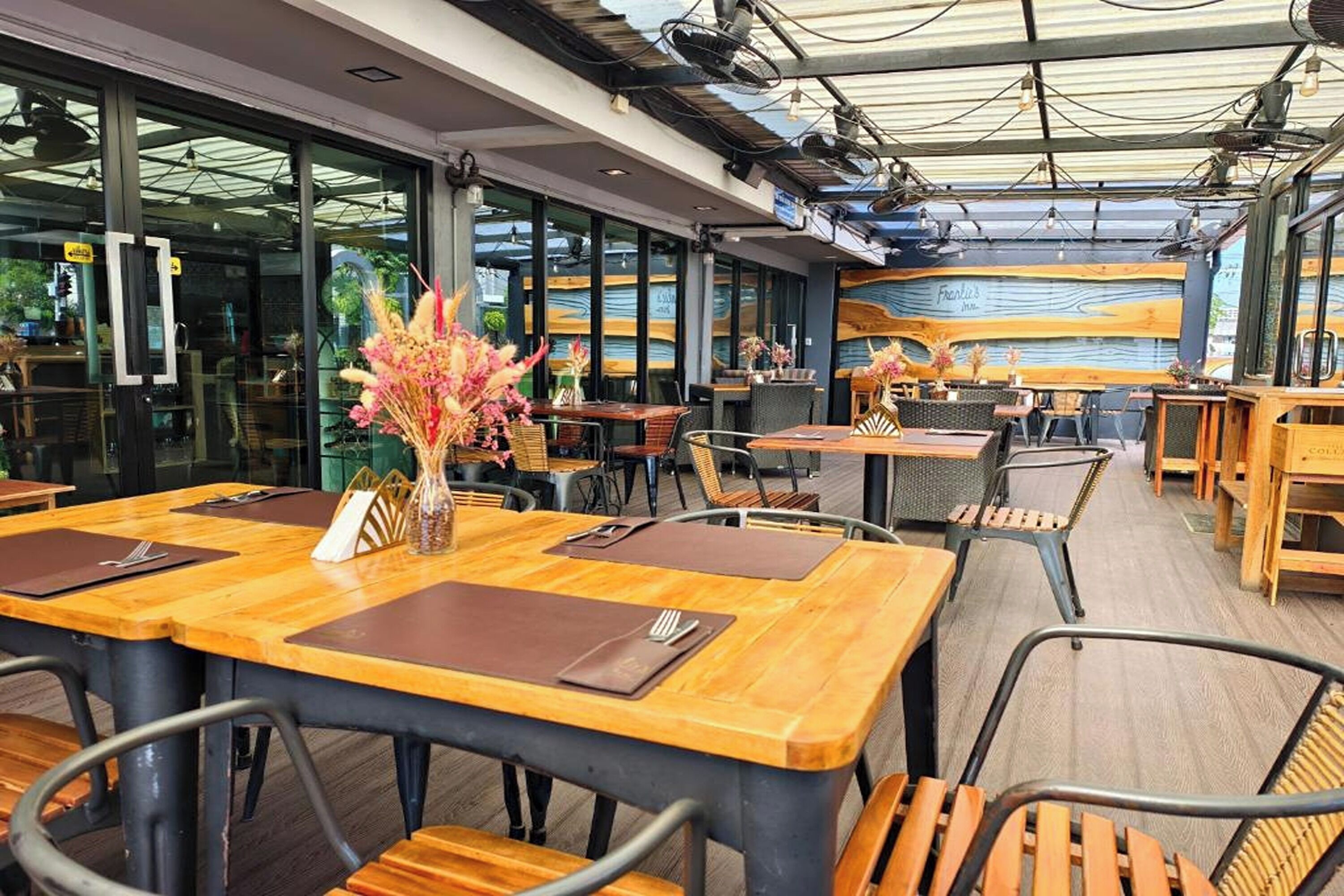 Un comedor interior con mesas y sillas de madera, ventanas amplias y un diseño moderno en el techo.