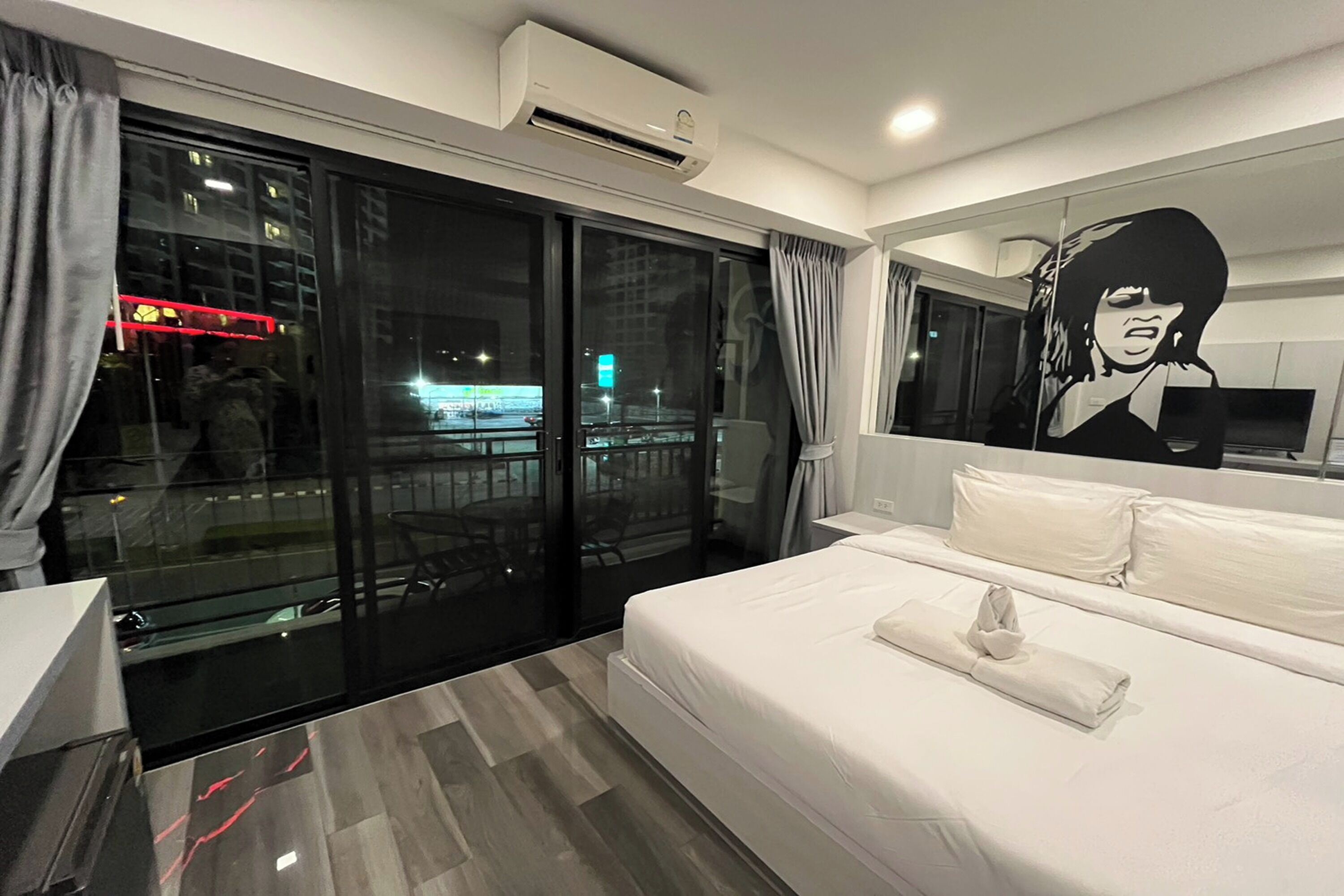 Habitación de hotel con una cama grande, una puerta de cristal que da a un balcón y un aire acondicionado instalado en la pared.